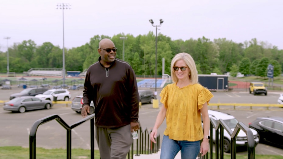 Dan and Molly, both wearing sunglasses, walk outside together.