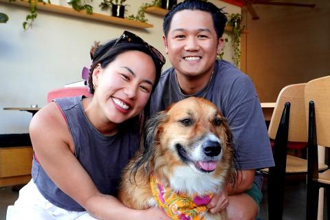 Angel smiles at the camera next to a dog and a smiling man.